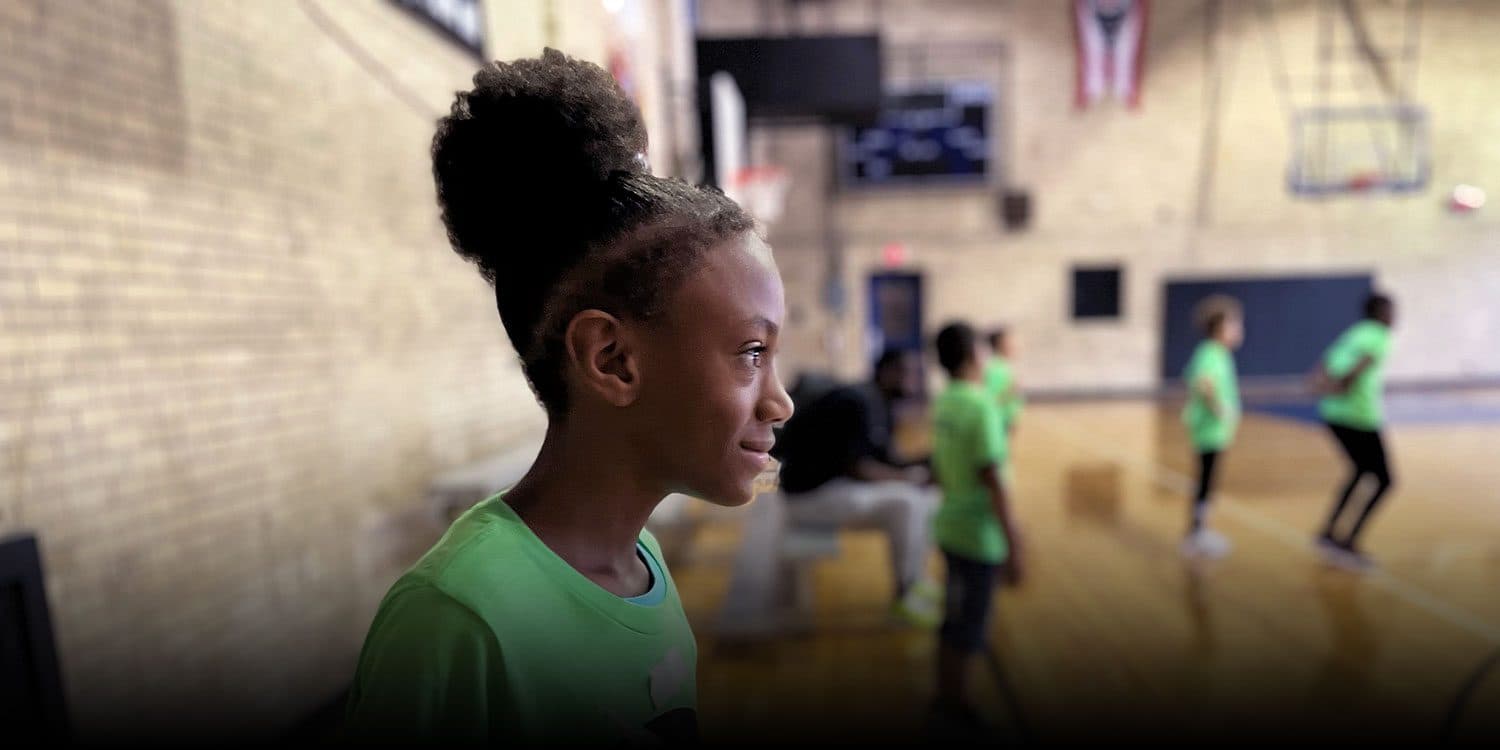Smiling student in a green shirt in the school gymnasium.