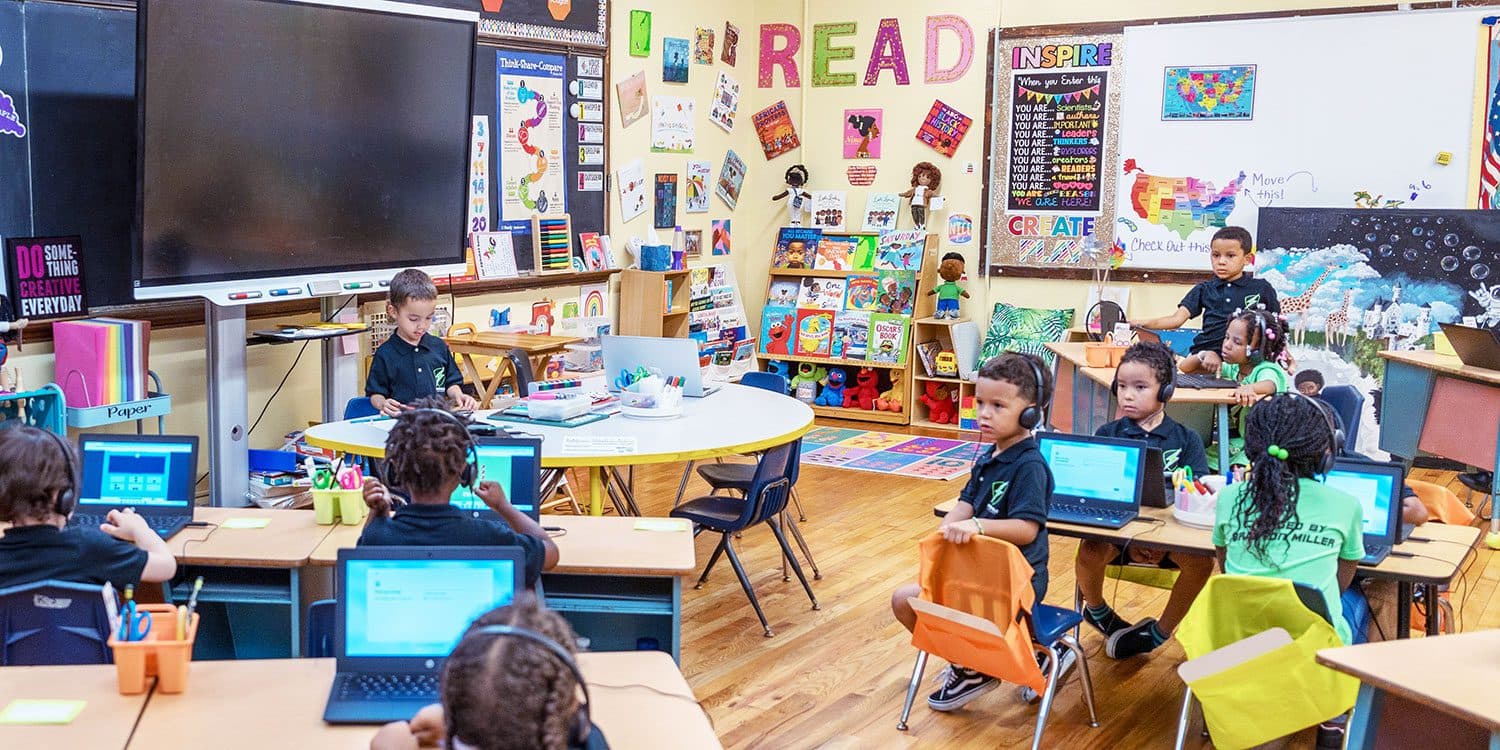 Students using laptops and headphones in a colorful classroom.