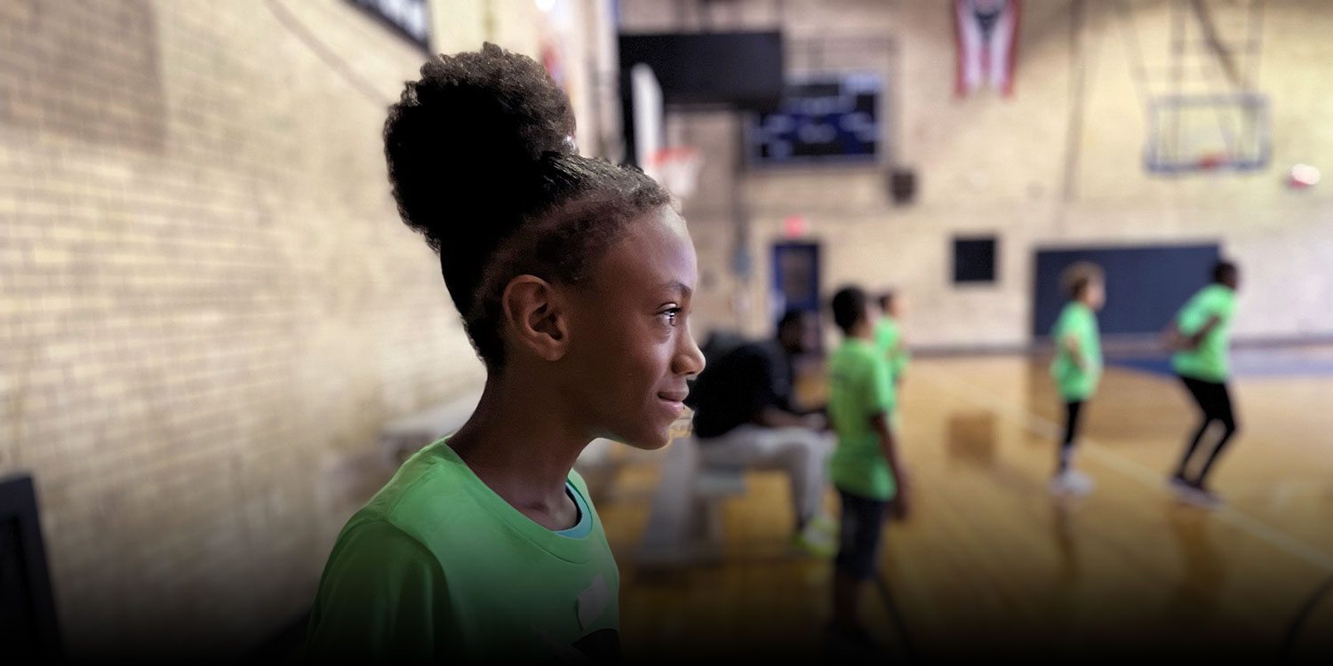 Smiling student in a green shirt in the school gymnasium.