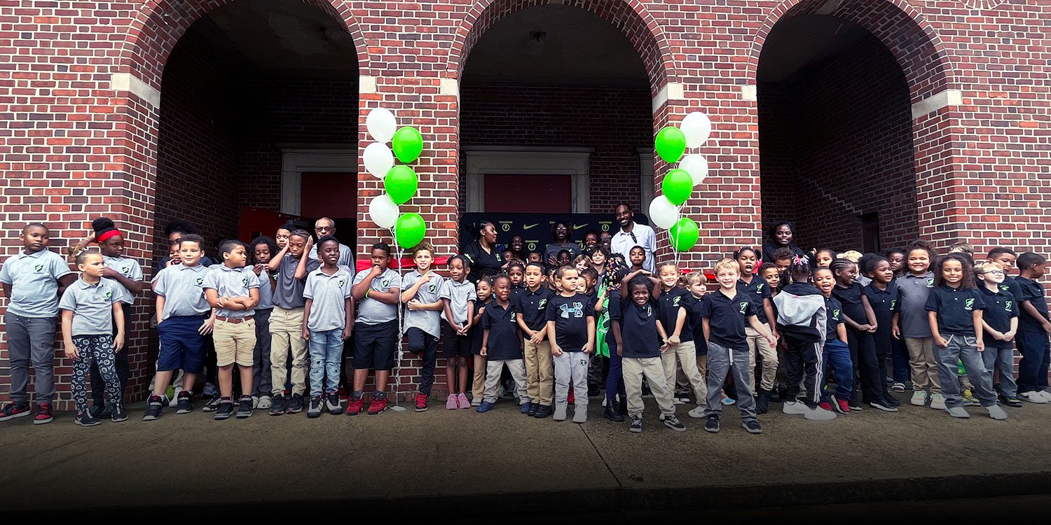 Students and staff gathered in front of the school's brick building with green and white balloons.