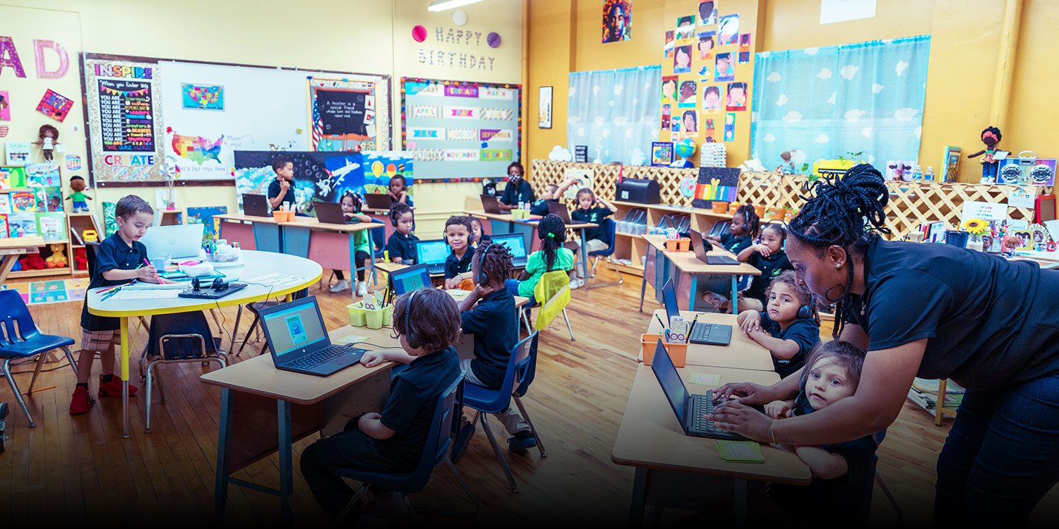 Students working on laptops with headsets on, with help from teachers
