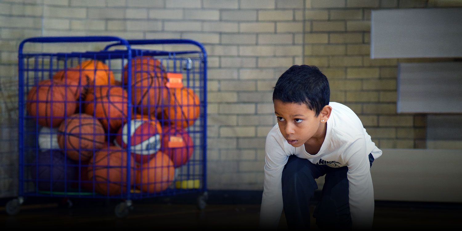 Student in school gym in a running stance with basketballs in the background
